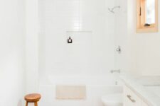 a serene white bathroom with white skinny and wood tiles, a vanity, a window, a tub and a wooden stool