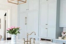 a serenity blue kitchen cabinets with white marble countertops and brass touches for a retro look