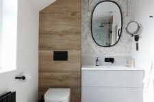 a small and chic bathroom clad with marble tiles, chevron and large scale ones, a wood look tile accent and black fixtures is stylish