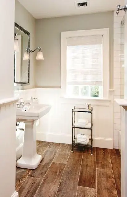 A small and lovely bathroom with light grey walls and paneling, a wood tile floor, a free standing sink and a shower space
