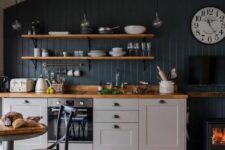 a small pretty kitchen with grey cabinets, a navy accent wall, open shelves, butcherblock countertops and a small hearth
