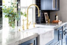 a stunning traditional kitchne in blue, with white stone countertops, a black tile backsplash and gold touches