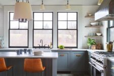 a stylish blue and grey kitchen with only lower cabinets, corner shelves, a cooker, a grey kitchen island, orange leather stools