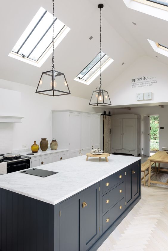 a stylish kitchen in white with a Victorian feel and a navy ktichen island, skylights and pendant lamps highlight the space