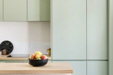 a subtle minimalist kitchen with sleek mint cabinets, a white kitchen island, butcherblock countertops and pendant bulbs