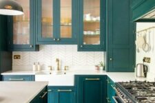 a teal kitchen with glass and usual cabinets, white countertops and a white tile backsplash, gold fixtures and handles