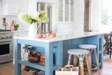 a traditional coastal kitchen with white cabinets, a blue kitchen island with a white countertop and blue rattan stools