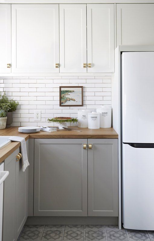 a two tone kitchen with white upper cabinets, dove grey lower ones, wooden countertops and gold handles
