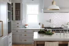 a vintage kitchen with dove grey cabinets, white tile backsplash, white lamps and wooden beams plus a kitchen island
