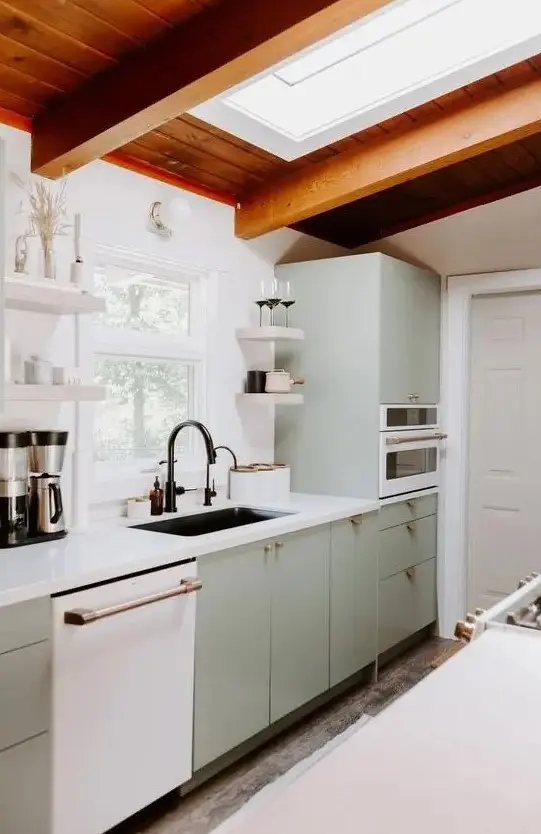 A welcoming mid century modern kitchen in light green, a skylight, a stained wood ceiling, white stone countertops