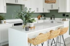 a white farmhouse kitchen with shaker cabinets and a kitchen island, a green backsplash and woven pendant lamps