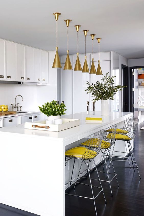 a white kitchen done with slight yellow accents - yellow stools and lemons in a bowl plus gold lamps over the island