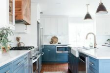 an airy kitchen with white and blue cabinets, white quartz countertops, a white backsplash and stainless steel handles plus a stained wooden hood