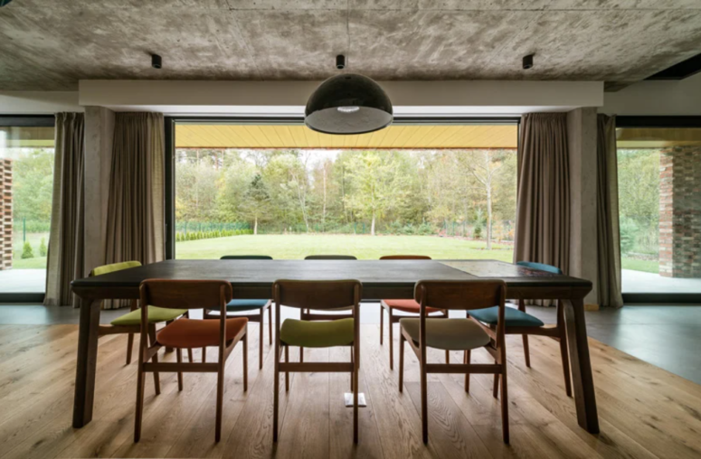 The dining space is placed in front of the window, with colorful chairs and a concrete ceiling that contrasts the warm decor