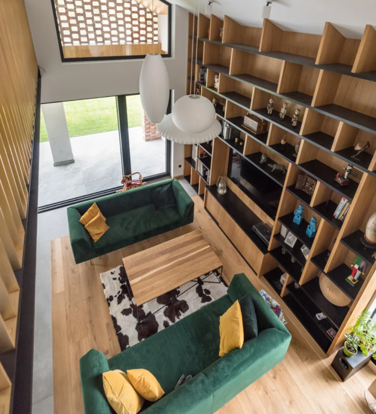 The living room is done with bold green sofas, yellow pillows, a large bookcase that takes a whole wall