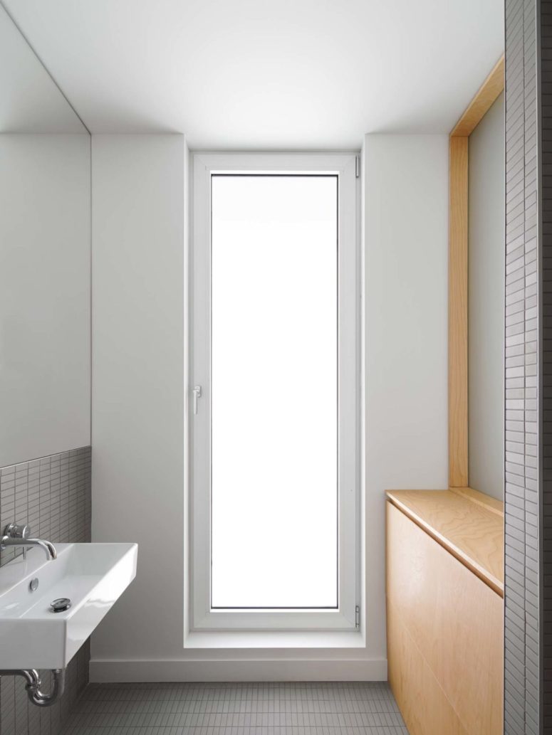 The bathroom is small, there's a frosted glass door, sleek plywood items and grey tiles on the walls and floor
