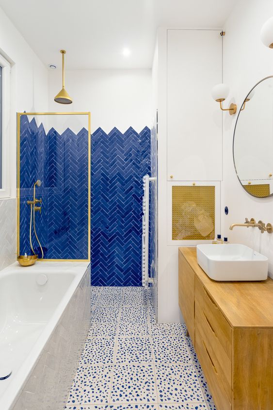 a bold bathroom with electric blue tiles, a dolmatin tile floor, a bold wooden vanity and a matching cover plus touches of gold