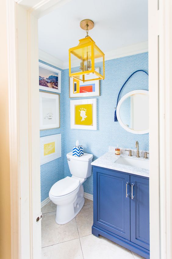 a bold powder room with blue penny tiles, a blue vanity, a yellow lantern and a pretty and bright gallery wall