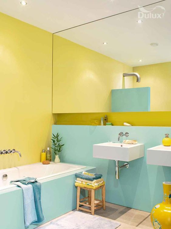 a bright color block bathroom in turquoise and yellow, with a large mirror, blue towels and sunny yellow touches