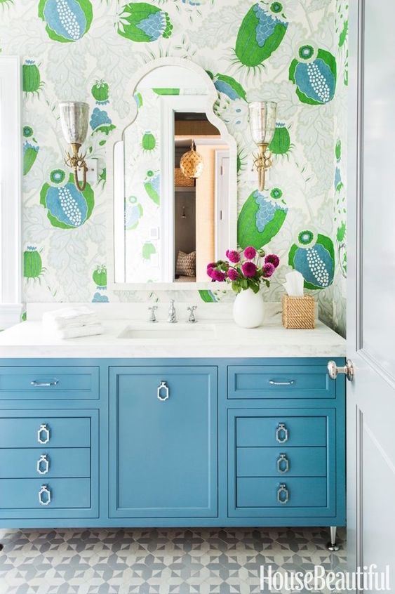 a bright bthroom with colorful and whimsical wallpaper, a blue vanity and bright blooms in a white vase