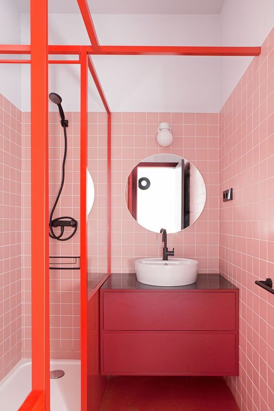 a bright modern bathroom with pink tile walls, a fuchsia floating vanity and orange frames is extra bold