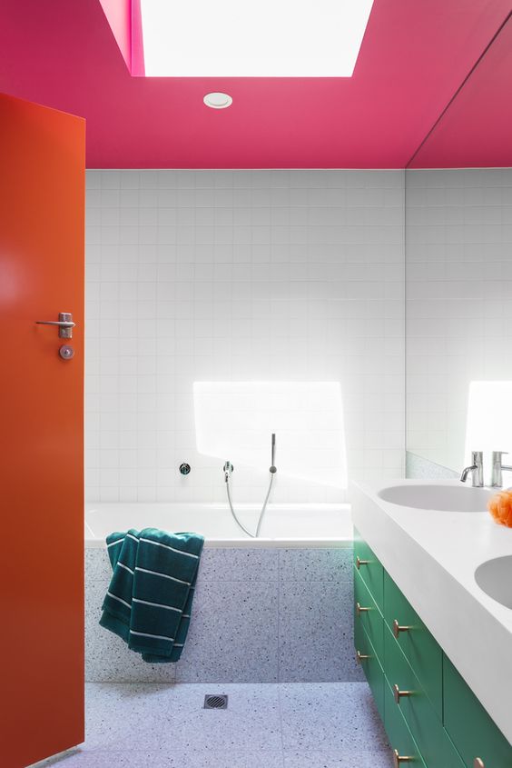 a colorful bathroom with a pink ceiling, an orange door and a green vanity with gold knobs is wow