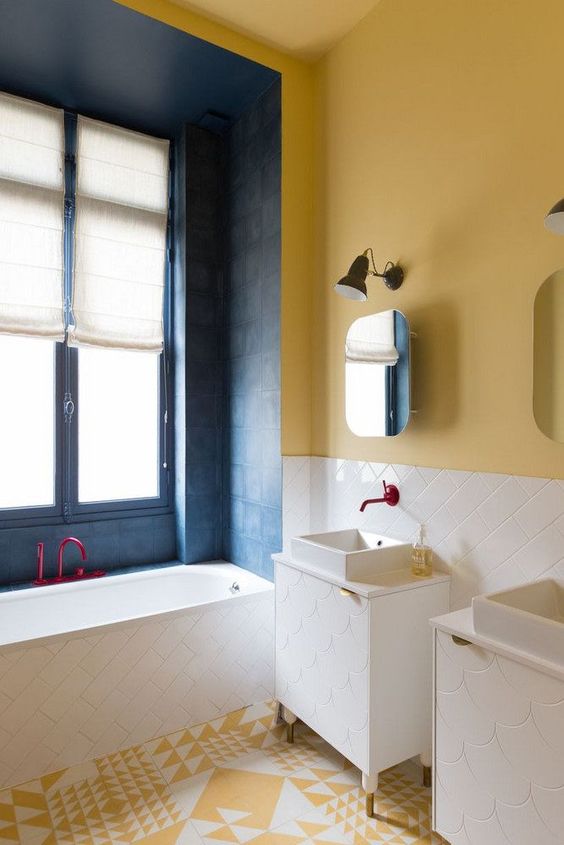 a colorful bathroom with yellow walls, a yellow and white mosaic floor and navy tiles around the bathtub plus fuchsia fixtures