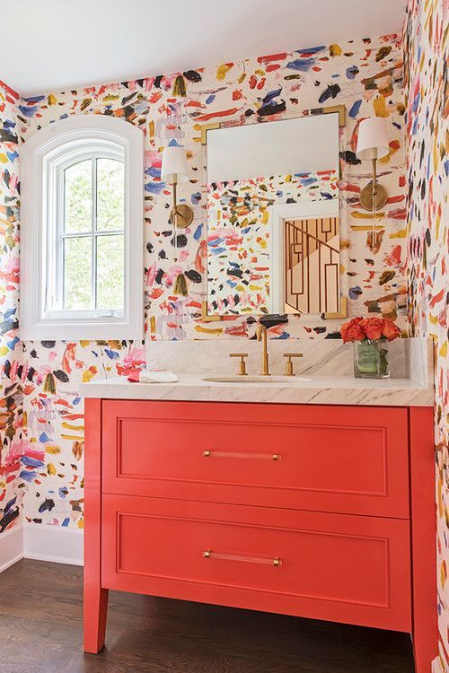 a super colorful bathroom with bright brushstroke wallpaper, a coral vanity and bright blooms in a clear vase