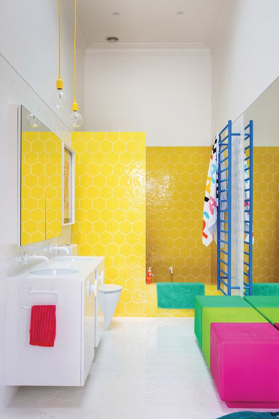 a super colorful bathroom with hex yellow tiles, colorful ottomans and bright textiles and a blue radiator