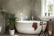 a beautiful grey bathroom with two kinds of tiles, potted plants, a free-standing tub, a candle lantern and a table
