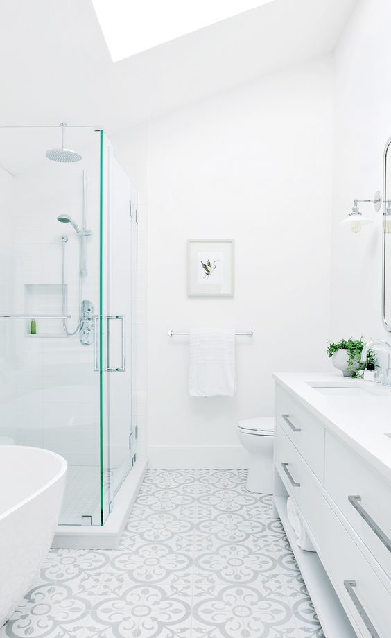 a beautiful white bathroom with a glass enclosed shower space, a large vanity, a mosaic tile on the floor and a large skylight