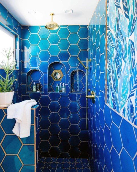 a bold blue bathroom clad with hex tiles and finished with gold grout and gold fixtures is a very chic space