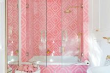 a bold contemporary bathroom with a tub space clad with bright pink tiles, gold fixtures and a mirror in a gold frame