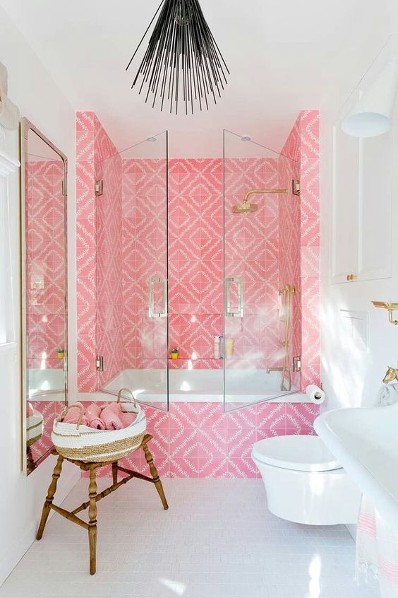 a bold contemporary bathroom with a tub space clad with bright pink tiles, gold fixtures and a mirror in a gold frame