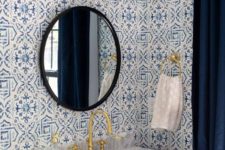 a bold powder room with mosaic tiles on the walls, a navy vanity, a stone sink, a sconce and a black framed mirror