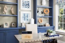 a bright blue home office with a large storage unit that takes a whole wall, a white industrial desk, a white chair and striped curtains