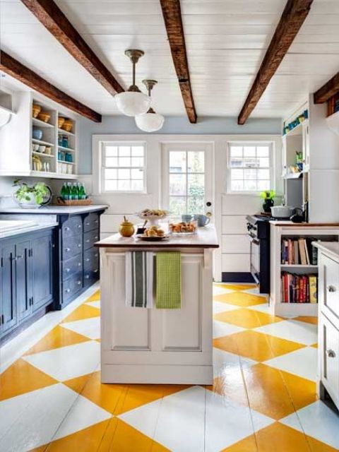 a bright kitchen with a geometric yellow and white floor, navy cabinets and dark stained wooden beams on the ceiling