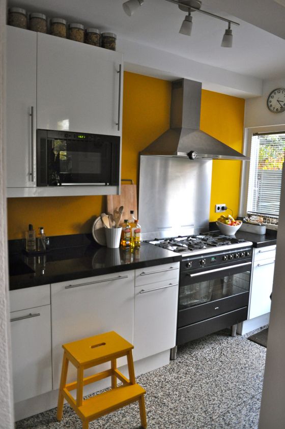 a bright kitchen with a mustard wall and a stool and black and white everything to calm that down a bit