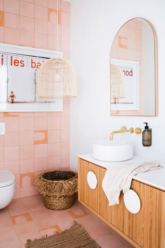 a catchy bathroom with pink tiles, a wicker lamp and basket, a floating vanity and gold fixtures for a glam touch