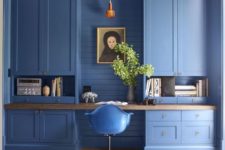 a catchy blue home office with large storage units, a built-in desk, a pendant lamp and greenery in a vase
