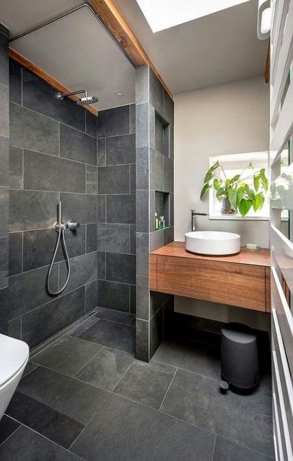a catchy modern bathroom clad with graphite grey tiles, with a built-in vanity, potted greenery and a skylight