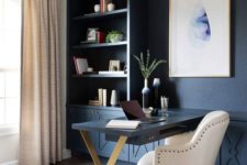 a chic home office with a blue wall taken by storage units, a statement artwork, a unique chandelier, a Murphy desk and a large white chair