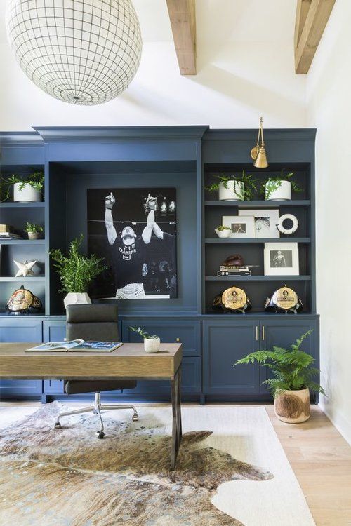 a chic home office with a whole wall in blue taken by a large storage unit, a wooden desk and a large lamp plus touches of gold