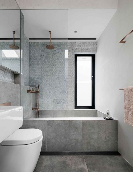 a chic minimalist grey bathroom with marble hex tiles, large scale grey ones and copper fixtures for a warmer touch