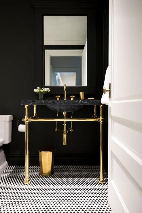 a chic powder room with black walls, a black marble sink, gold fixtures and legs plus a mosaic tile floor