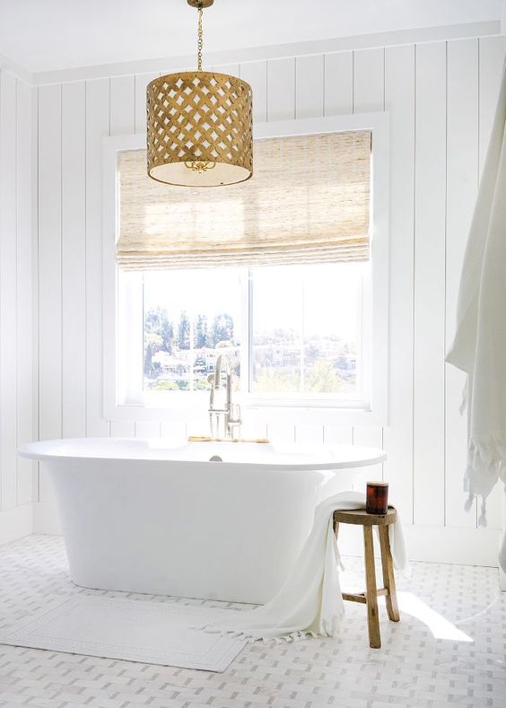 a chic white bathroom with shiplap walls, a mosaic tile floor, a tub by the window and a fabric covered vanity