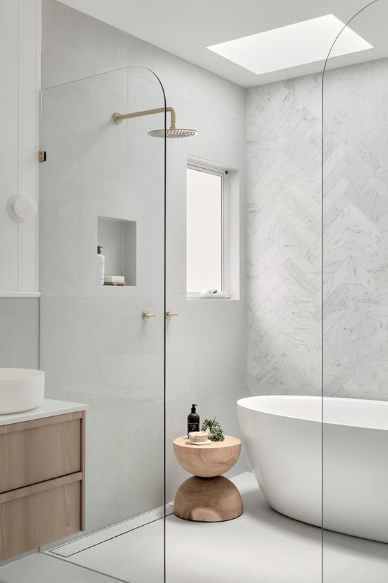 a clean white bathroom with a window and a skylight, a shower space with a tub, a stained vanity, gold fixtures and a cork side table