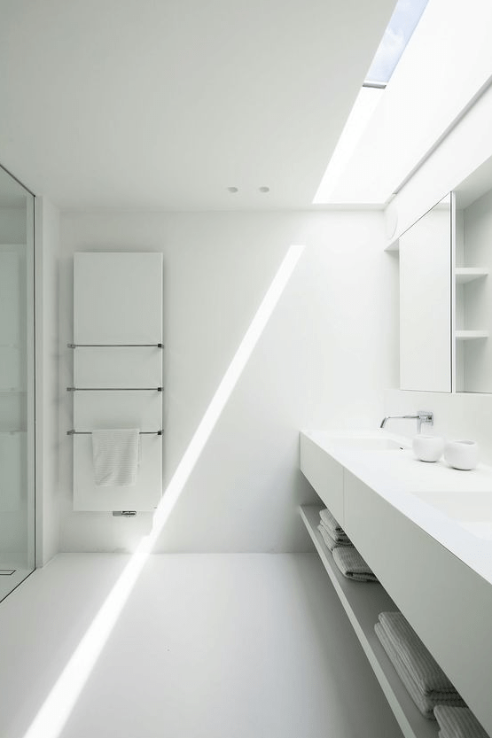 a clean white minimalist bathroom with a skylight, a floating vanity, a statement mirror cabinet and stainless steel fixtures