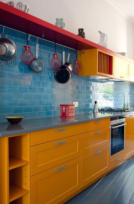 a colorful modern kitchen with yellow cabinets, a blue tile backsplash and touches of bright red for more boldness
