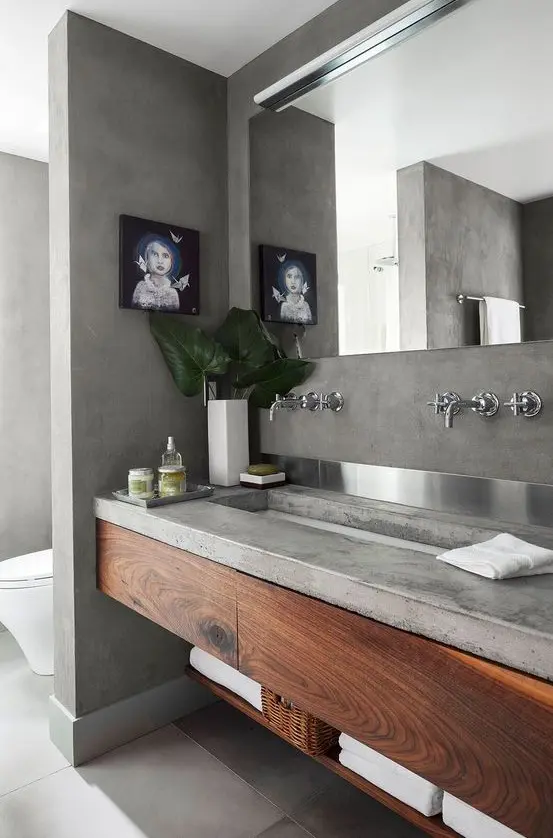 a concrete bathroom with a concrete vanity and wooden storage units, a large mirror and a window to enjoy natural light